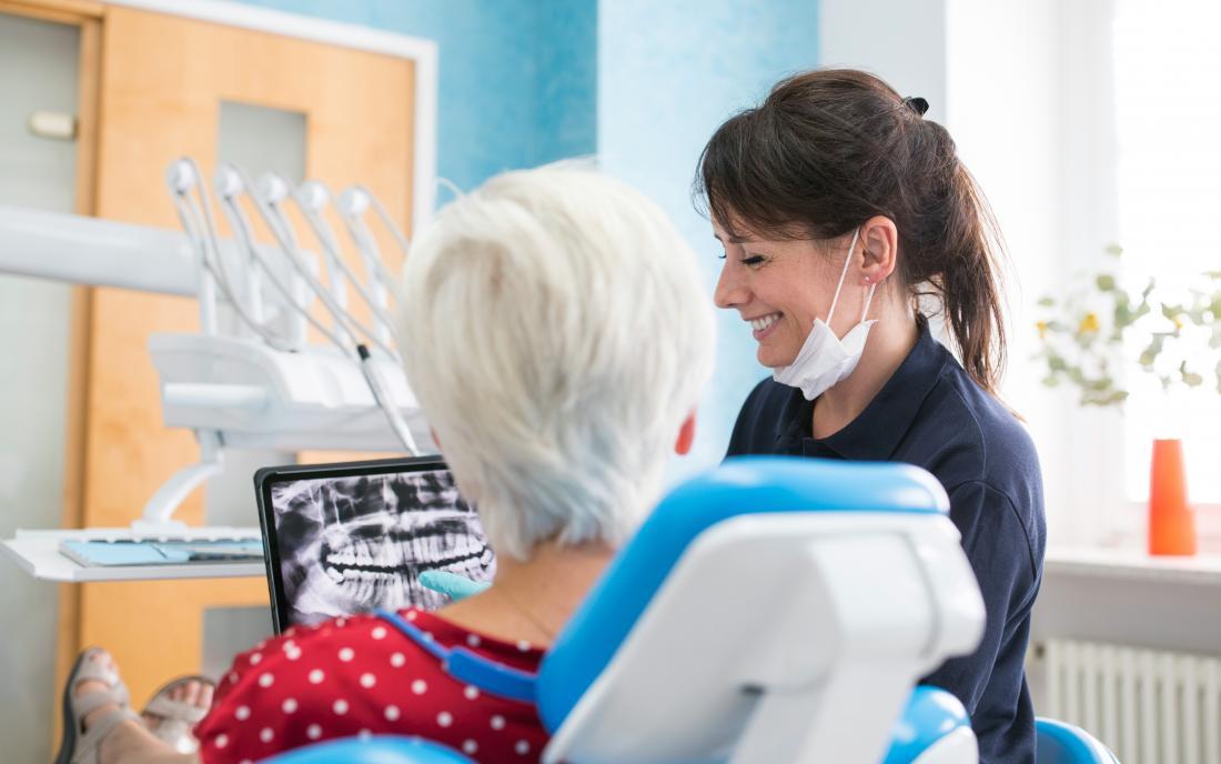 a dentist showing a lady an x-ray of her mouth and pointing towards where a Tooth extraction will happen.