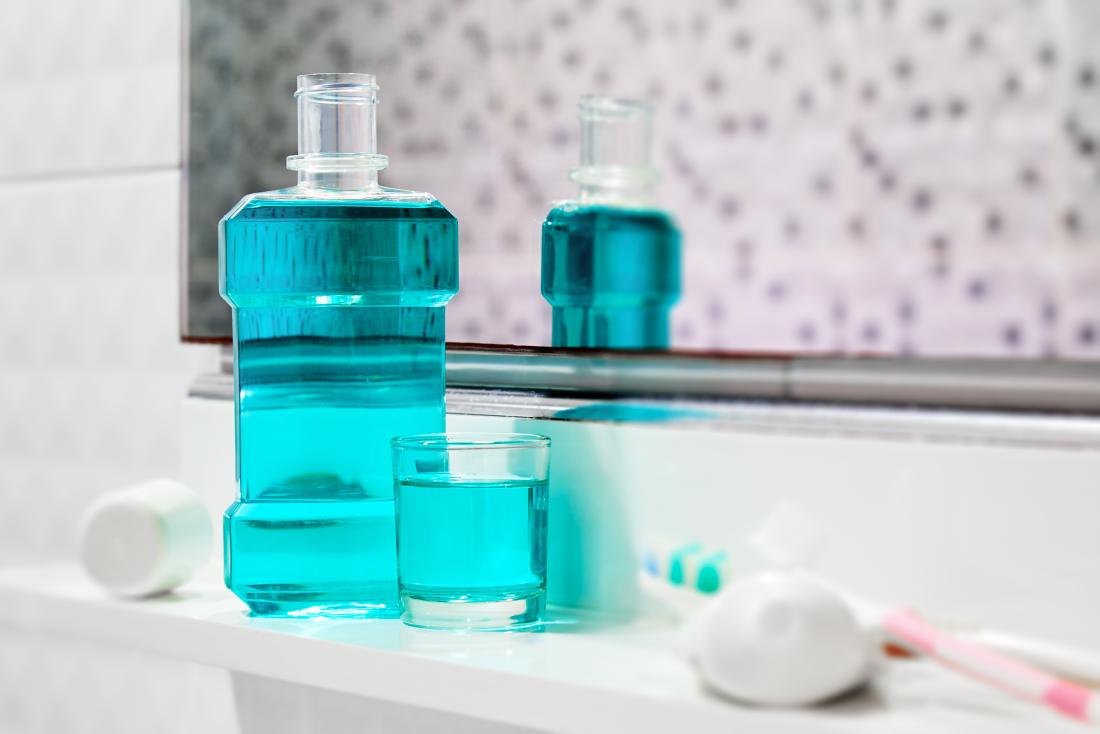 Antiseptic mouthwash and toothpaste on bathroom shelf in front of mirror.