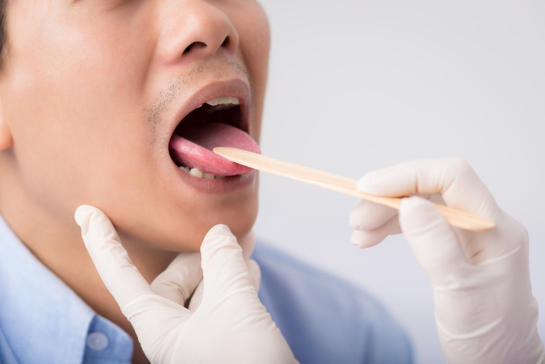 Doctor inspecting tongue and throat of patient.