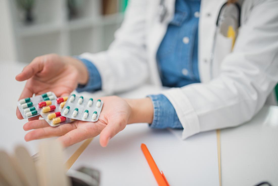 Doctor with multiple packets of pills, medication, and drugs in hands being offered to patient.