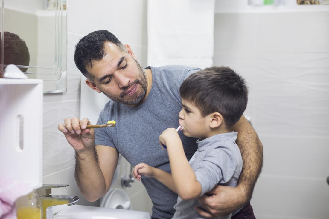 Father helping son clean his teeth