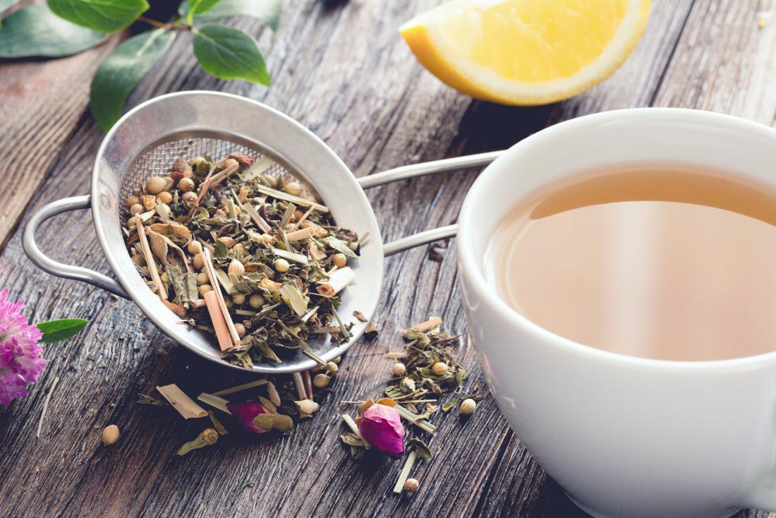 Herbal loose leaf tea on wooden table with strainer and orange or lemon slice