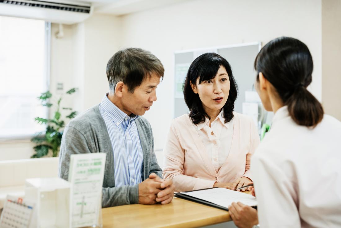 Man and woman at reception desk in clinic waiting room signing papers.