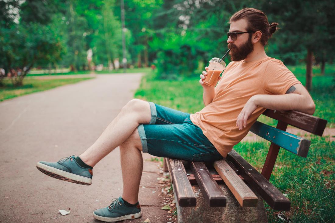 man sitting on bench in park drinking smoothie through straw