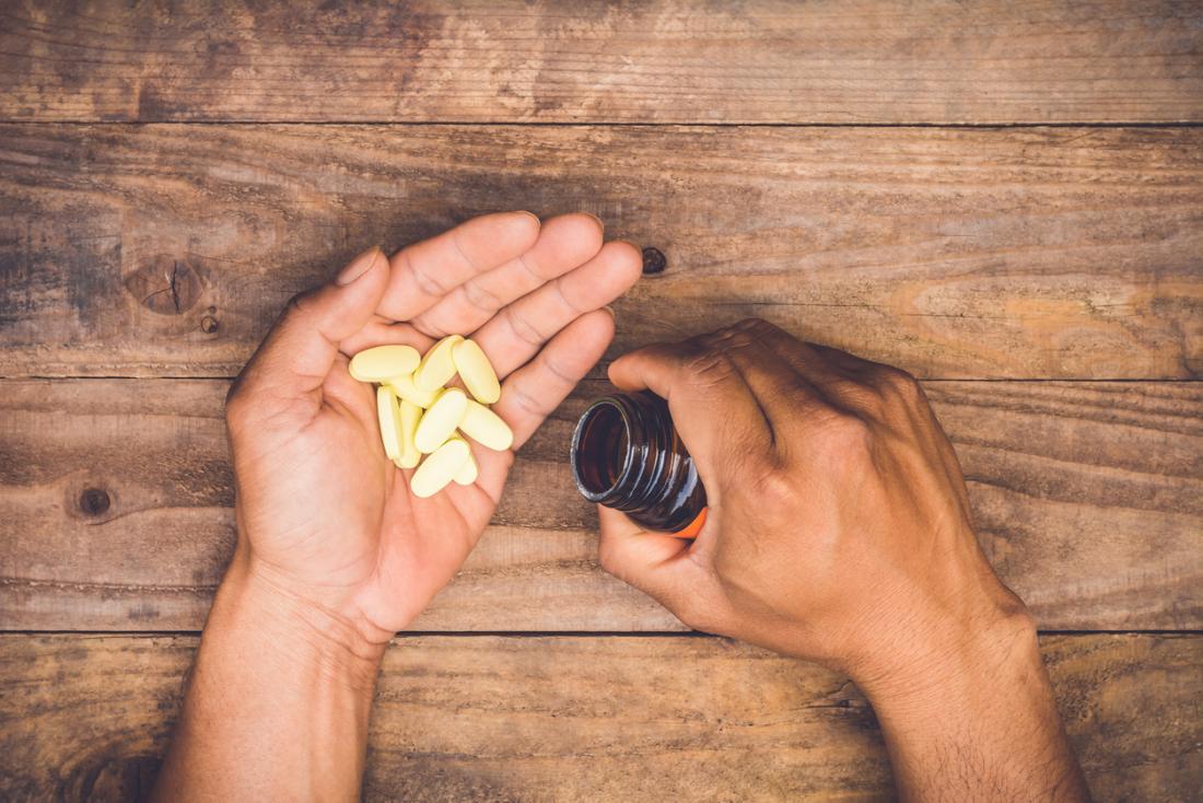 Person emptying multivitamin pills from bottle onto palm.