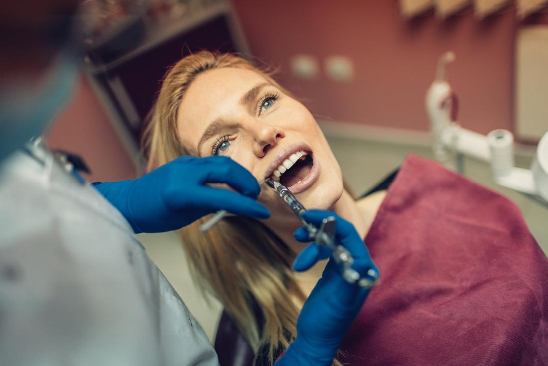 Woman receieving novocaine anesthesia from dentist during operation.