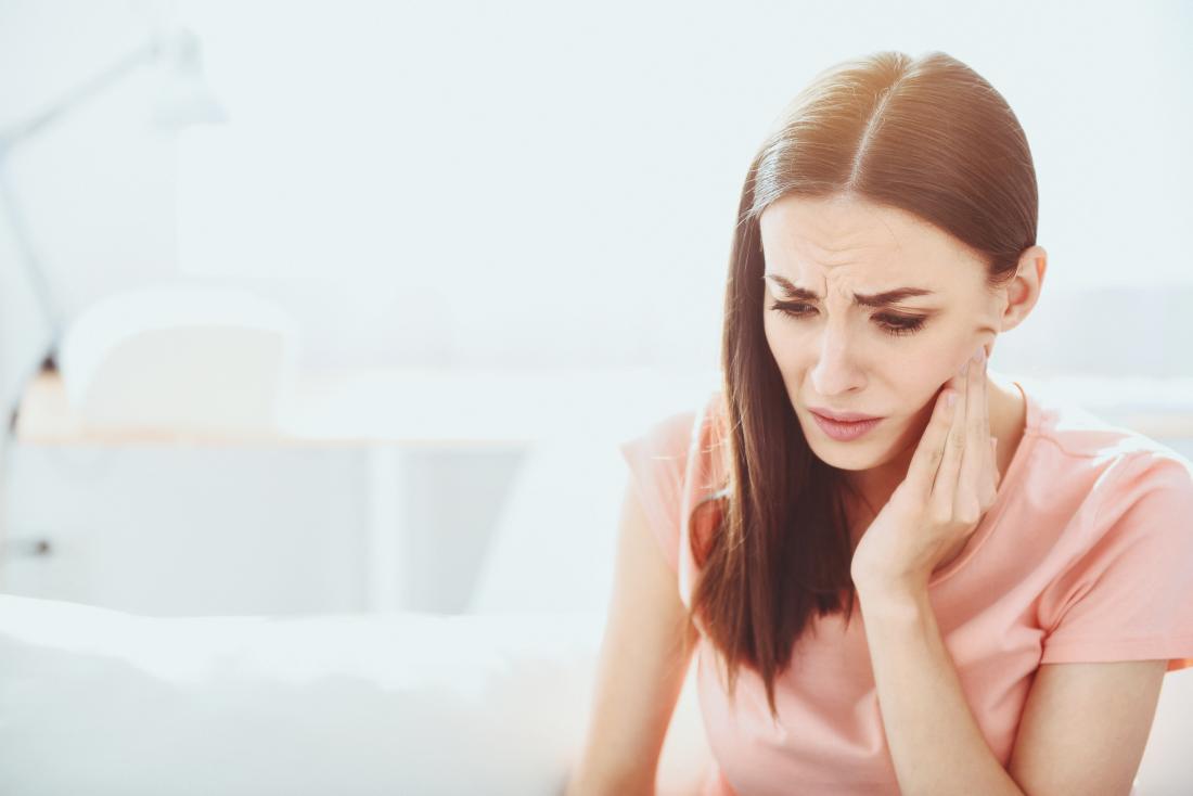 Woman with wisdom tooth ache holding side of mouth in pain.